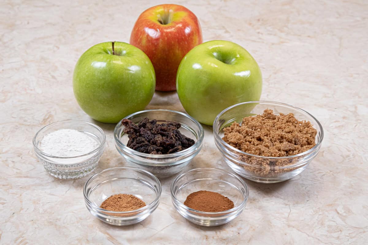 The apple filling for the Apple Crisp Cheesecake includes apples, raisins, brown sugar, flour, cinnamon, and nutmeg.