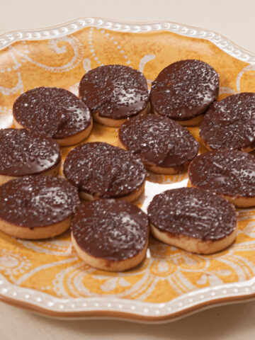 Round butter cookies finished with chocolate on an orange and white plate.
