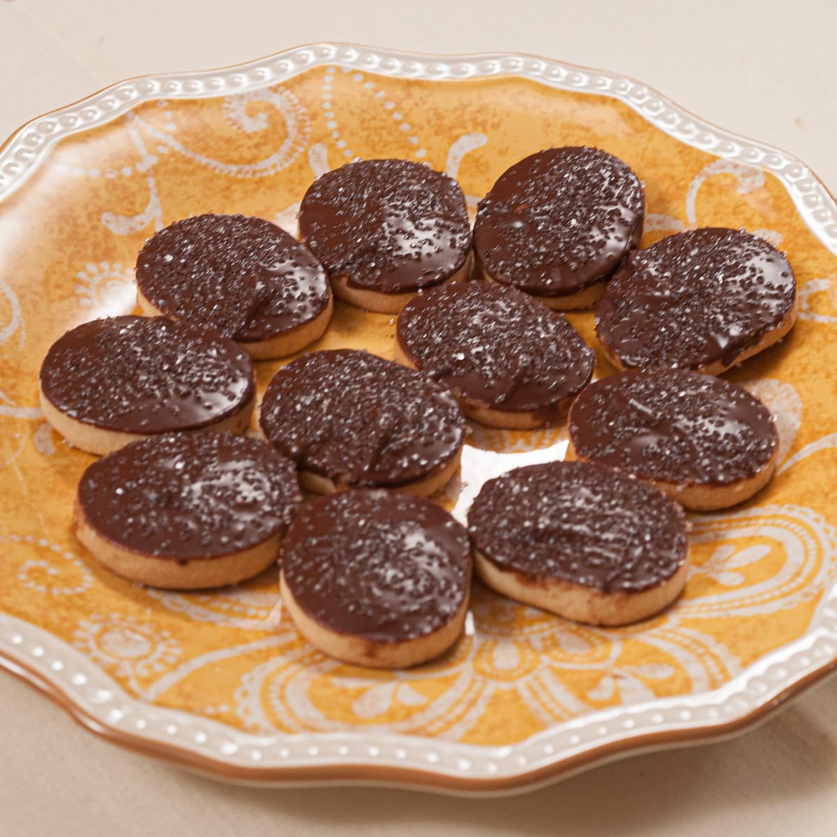 Round butter cookies finished with chocolate on an orange and white plate.