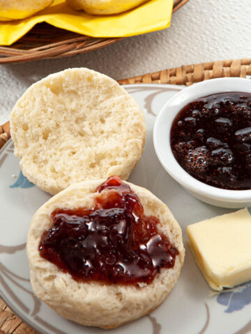 A Cream Biscuit split open with strawberry balsamic jam. A pat of butterr and a dish of jam sit on the plate with the biscuit.