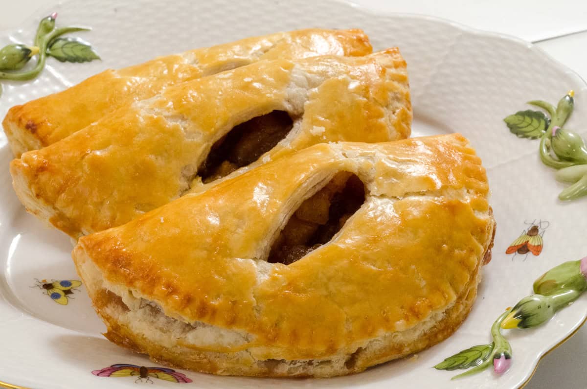 Three golden half moon hand pies with slits showing the apple filling sit on an Irish decorated platter.