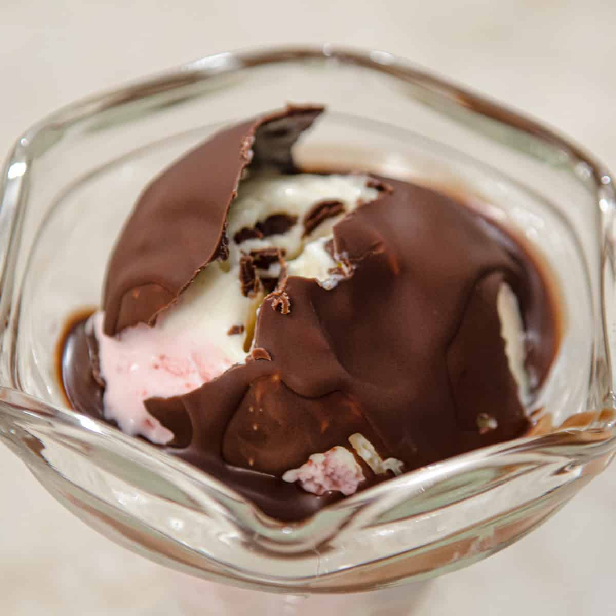 Ice cream in a sundae glass is covered with a broken chocolate Magic Shell.