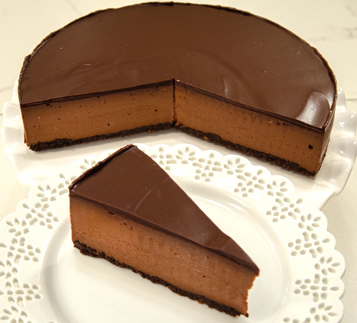 A slice of Triple Chocolate Cheesecake with the cheesecake in the background.