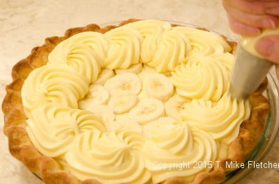 Piping the pastry cream over the bananas for the Double Banana Caramel Cream Pie