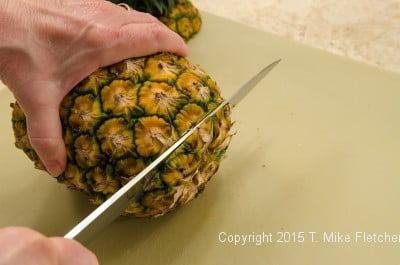 Cutting the bottom of the pineapple off for the Pina Colada Cake