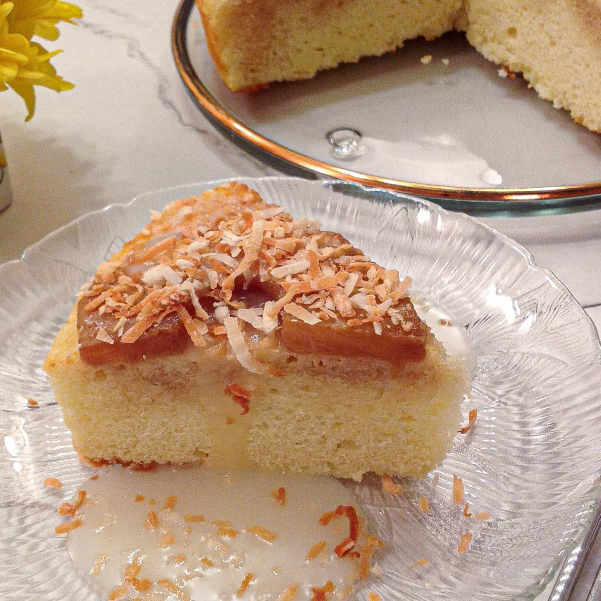 A slice of the Pina Colada Cakes sits on a clear plate with sauce on the side and the remaining cake in the background.
