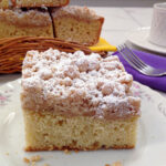 A piece of the New York Crumb cake on a plate with a stack in the background.