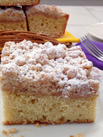 A piece of the New York Crumb cake on a plate with a stack in the background.