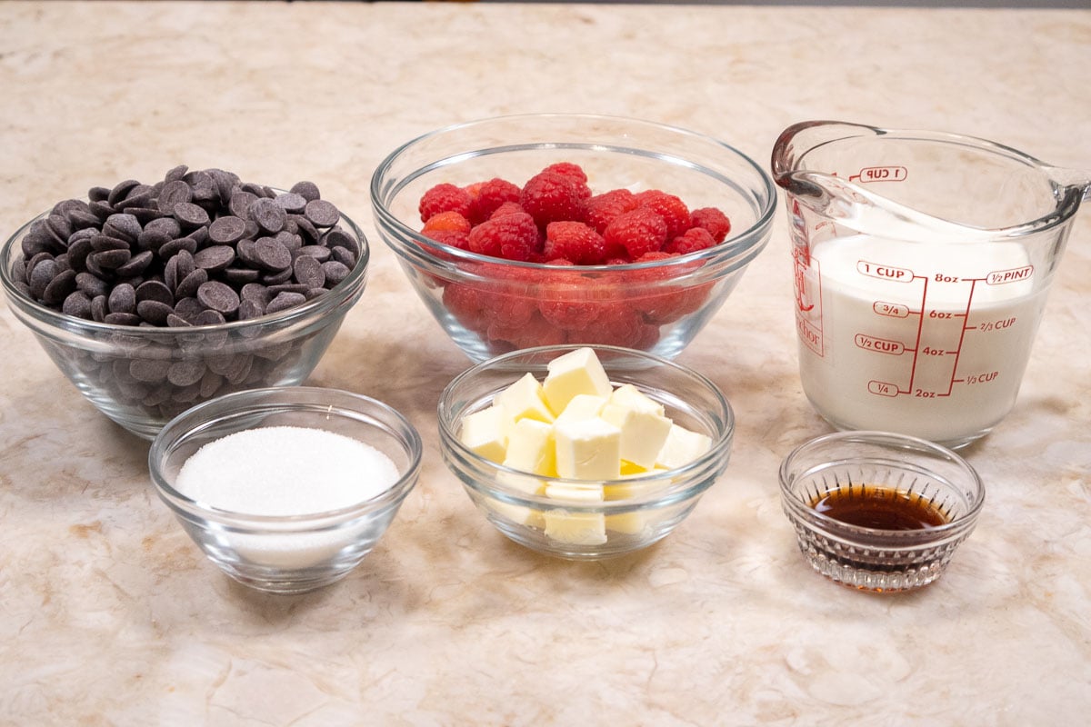 Ingredients for the Chocolate Raspberry Truffle Tart Filling include in the back row, chocolate, fresh raspberries and cream.  In the front row are sugar, butter and vanilla
