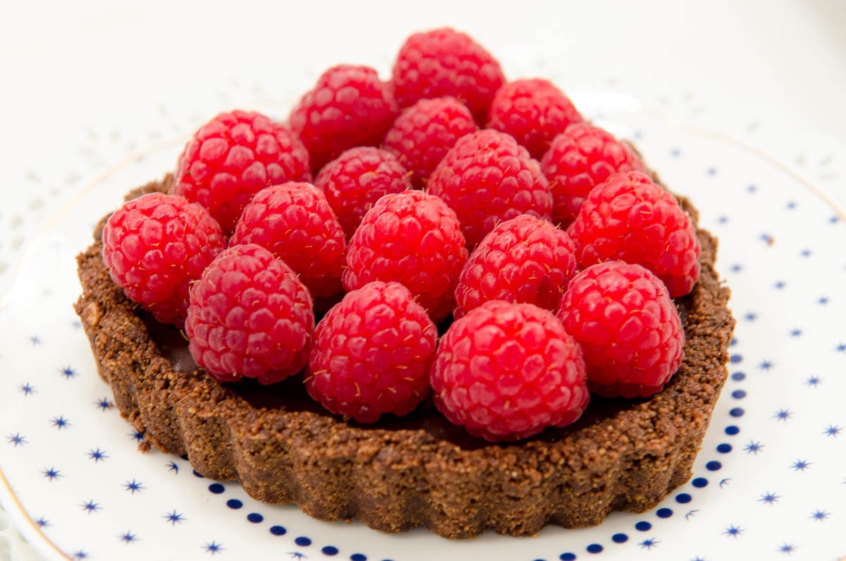 The tart if finished with fresh raspberries and ready to serve on a white plate with blue dots.