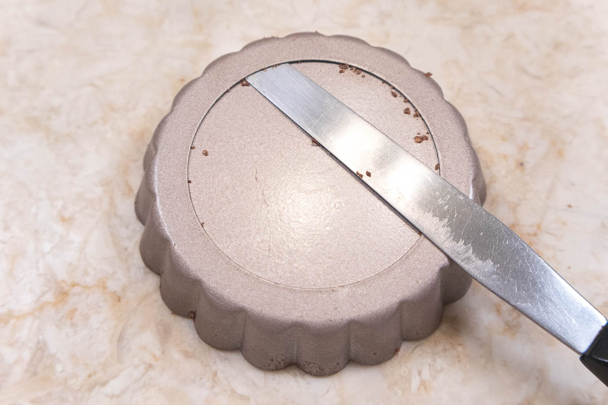 A small, flexible spatula is placed under the bottom rim of the tart pan.  It goes around the entire edge of the pan.