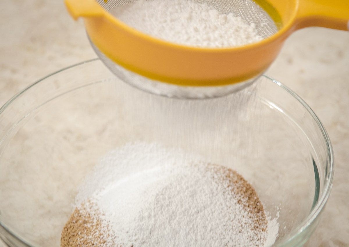 The powdered sugar is placed in a strainer and sifted over the graham cracker crumbs