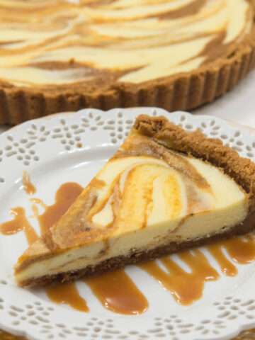 A slice of Pumpkin Cheesecake Tart on a plate with Rum Caramel Sauce and the tart in the bakground