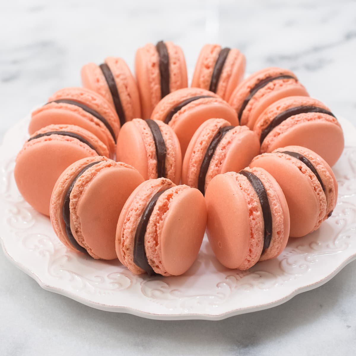 Pink macarons filled with chocolate and raspery on a white plate.