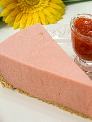 A slice of the Rhubarb Cream tart with a small carafe of strawberry sauce with a green napkin and yellow daisy.