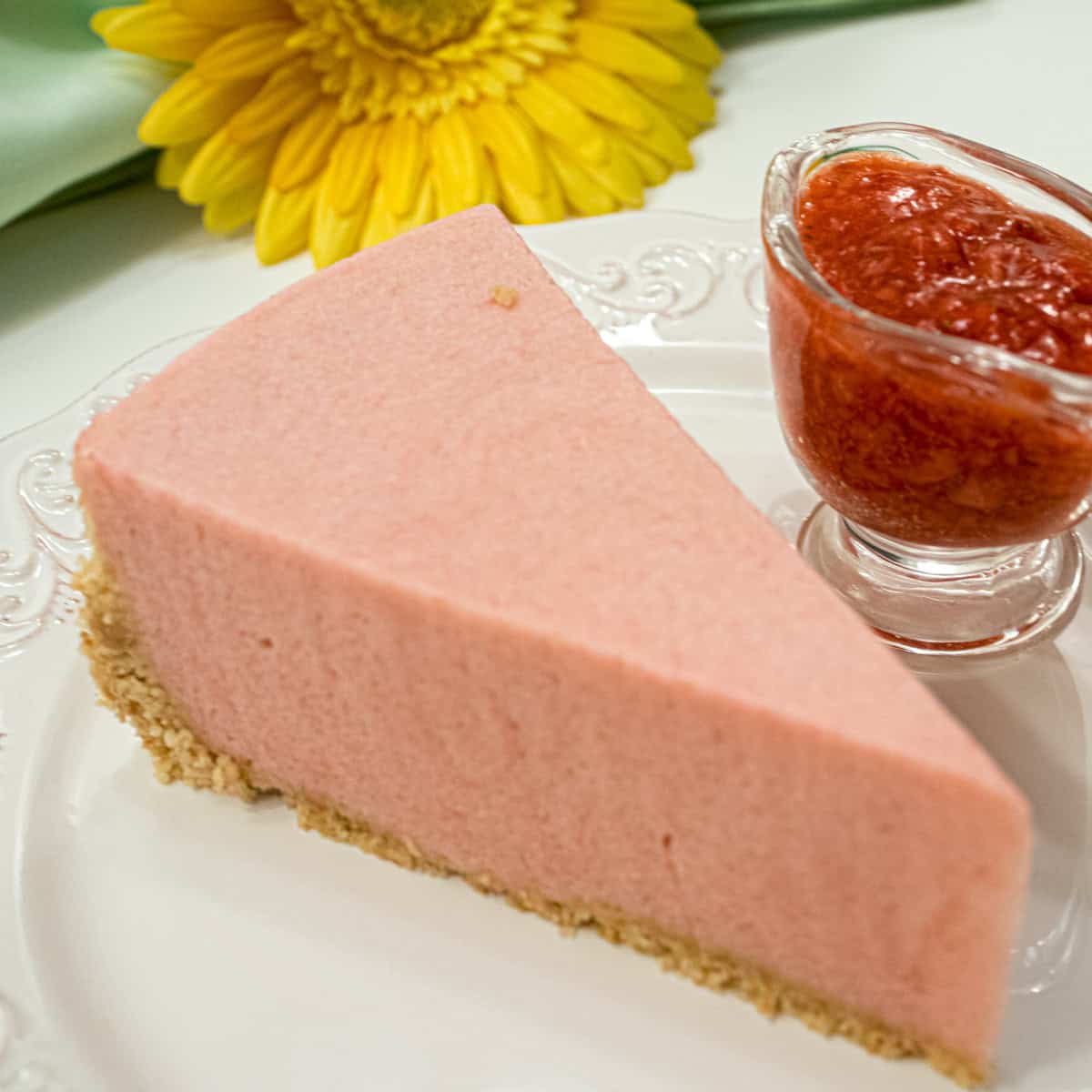 A slice of the Rhubarb Cream tart with a small carafe of strawberry sauce with a green napkin and yellow daisy.