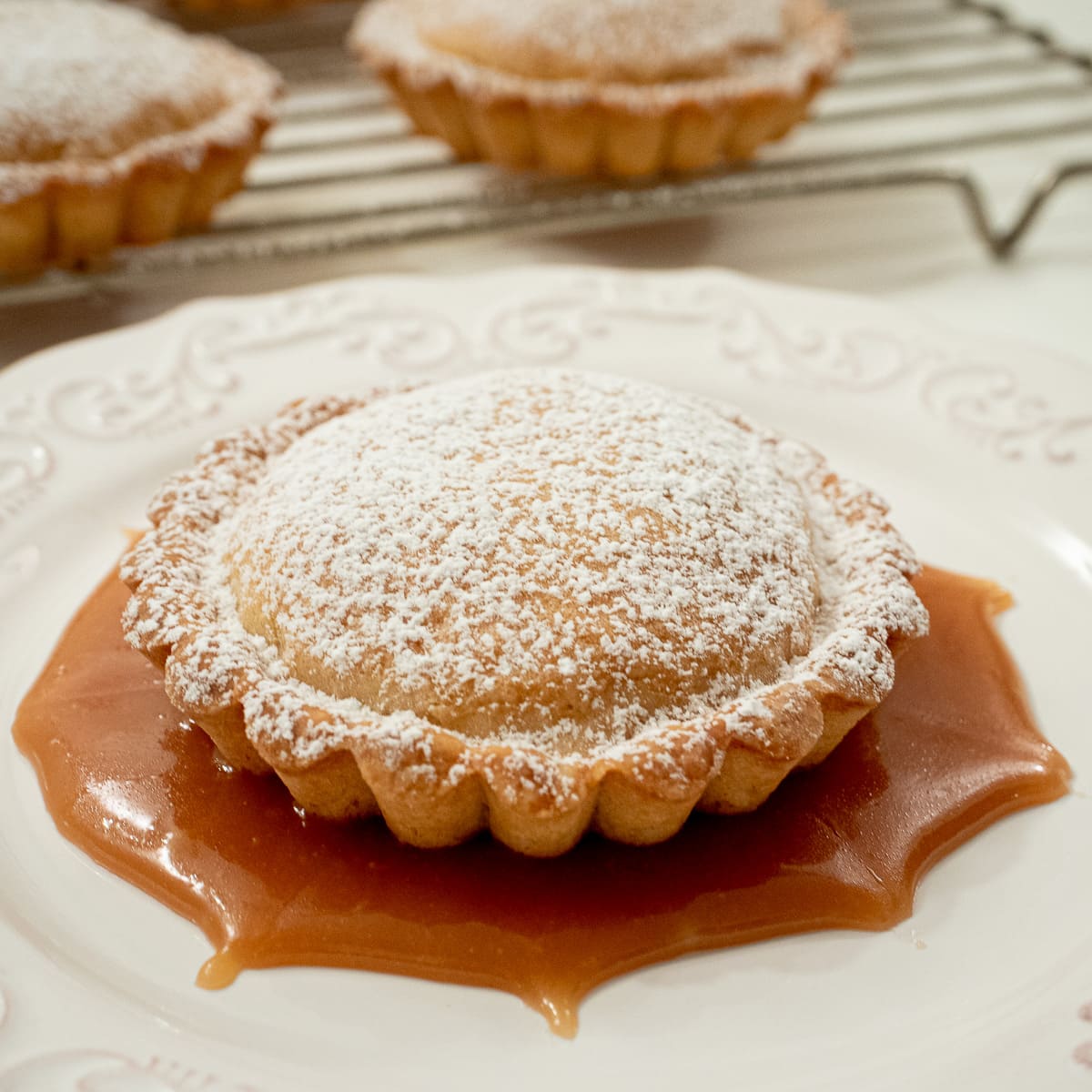 These individual Brown Butter Tarts feature a butter crust filled with brickle bits and a browned butter filling.  They are lightly dusted with powdered sugar and served with caramel sauce