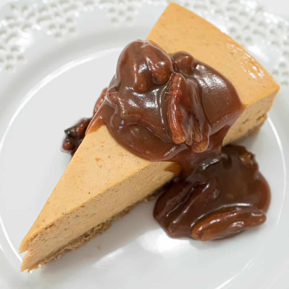 A slice of the Pumpkin Cheesecake with Salted Caramel Sauce sits on a white plate with a lace edge.