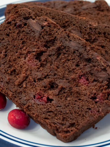 Slices of Chocolate Cranberry Quick Bread served on a blue rimmed white plate with several fresh cranberries on the plate