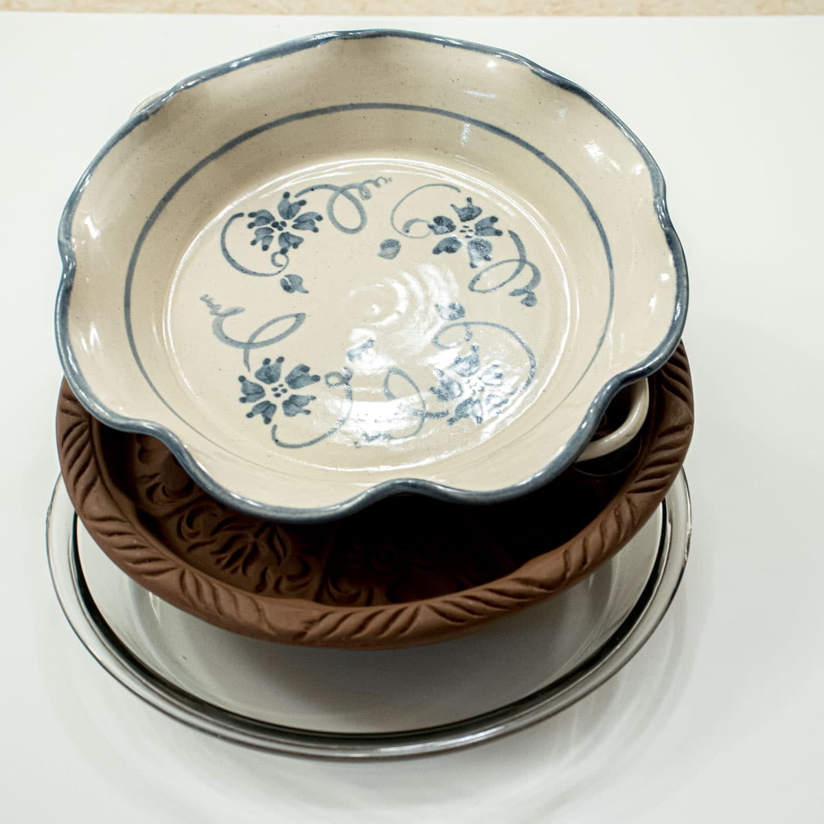 Three different compositions of baking pans are featured - a 9" glass pie plate, a 9"decorative clay shortbread mold, and a ceramic blue and white pie plate