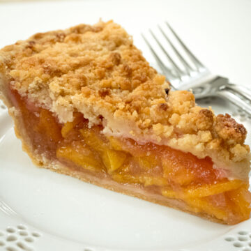 A slice of Dutch Peach Pie on a white lace plate with a fork beside it.