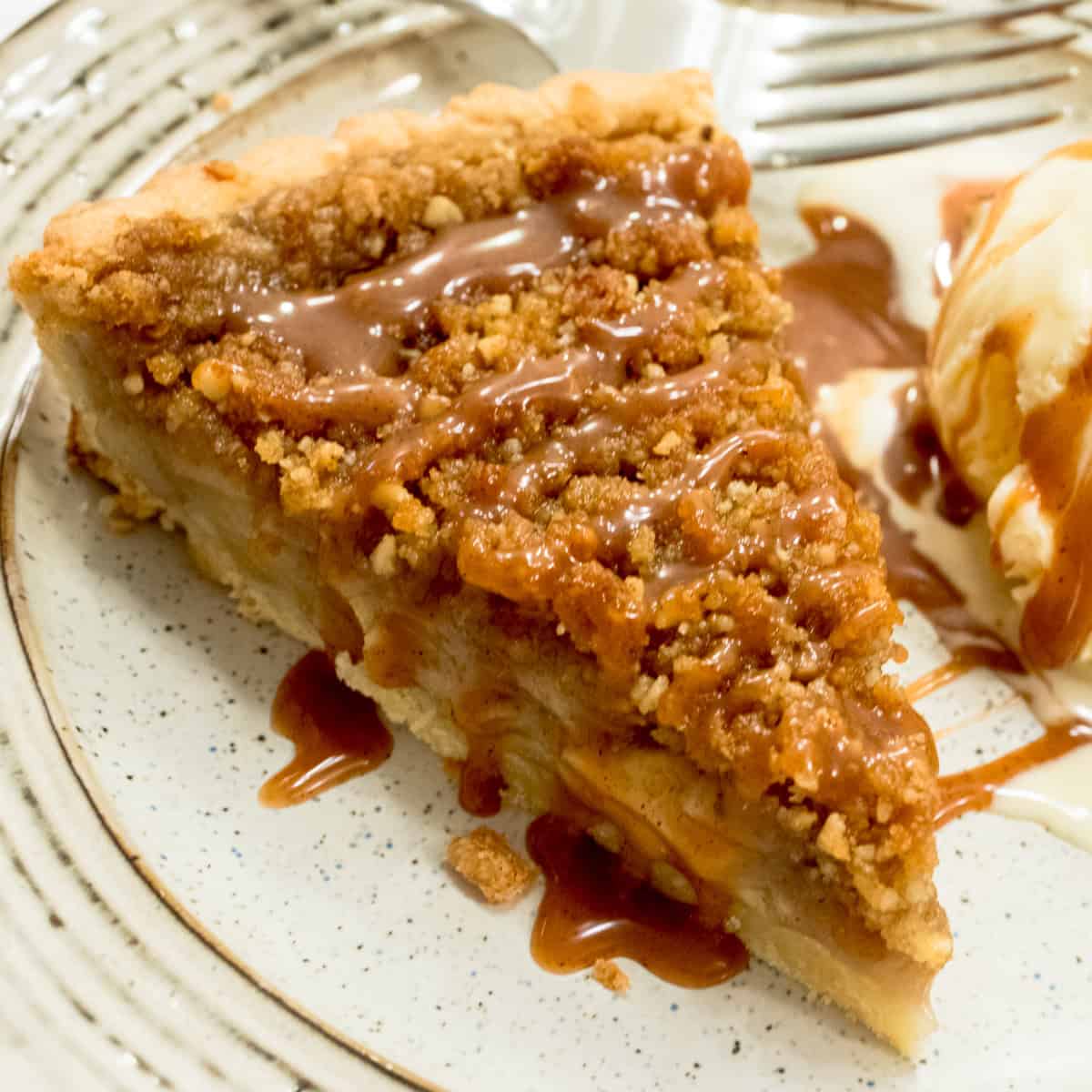 A slice of the Cinnamon Whiskey Tart sits on a plate with a scoop of ice cream and caramel sauce.