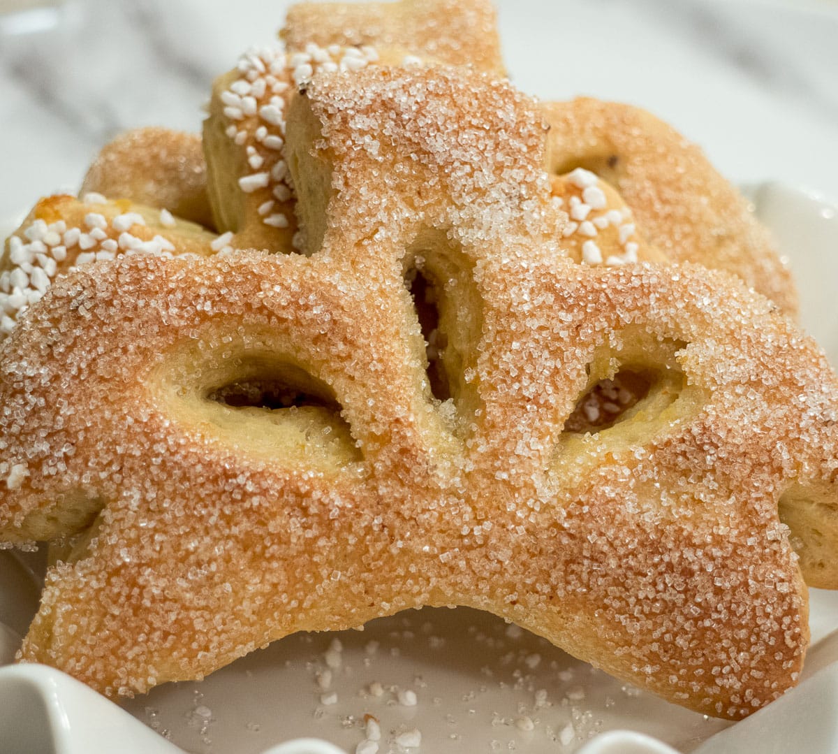 This Gibassier which sits on a white plate is a French breakfast sweet roll in the shape of a fleur de lis.