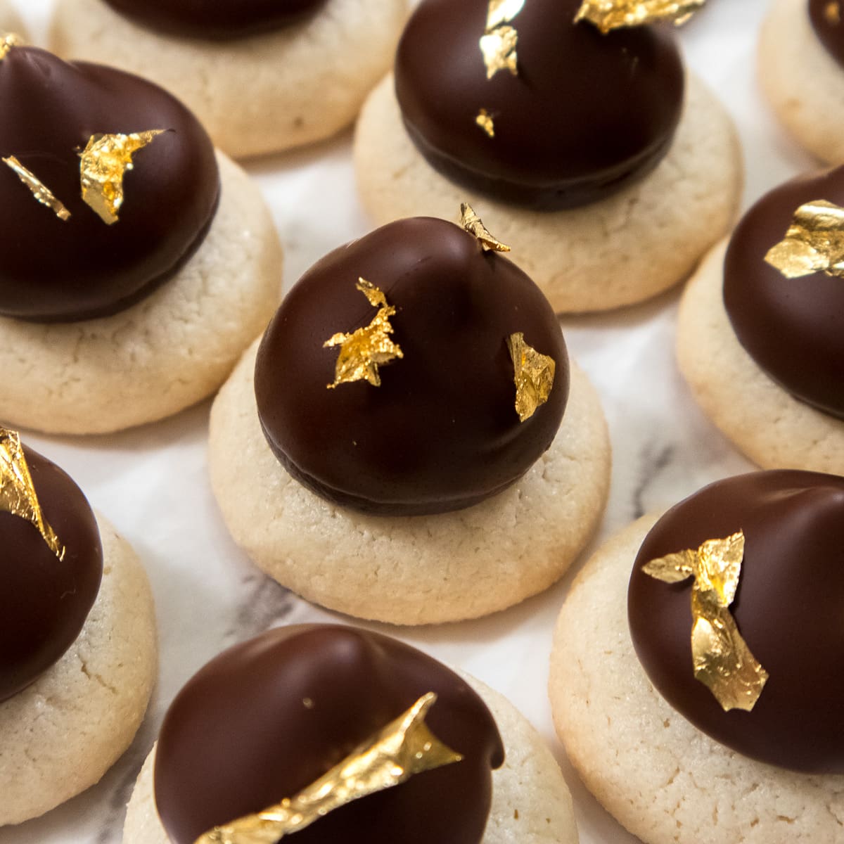 Sarah Bernhardt cookies feature a macaron base with a chocolate ganache filling,dipped in chocolate and finished with gold leaf