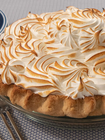 A meringue topped coconut cream pie in a glass pie pan with plates and forks beside it.