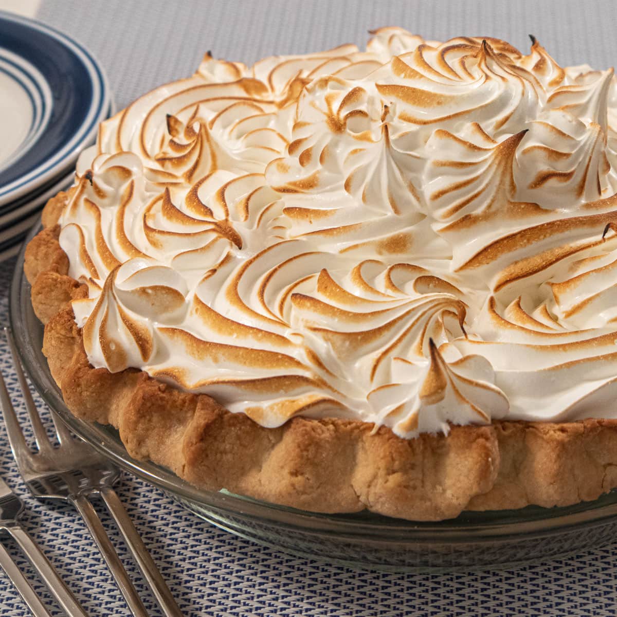 A meringue topped coconut cream pie in a glass pie pan with plates and forks beside it.