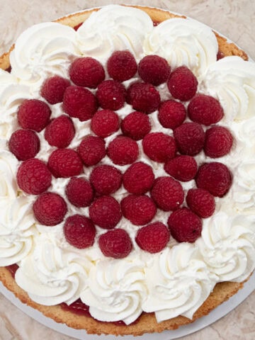 A Quick and Easy Summer Cake shot from the tp with a wreath of whipped cream holding fresh raspberries.