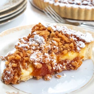 A slice of the Caramelized Peach Tart sits on a antique plate with more plates and the tart in the background.