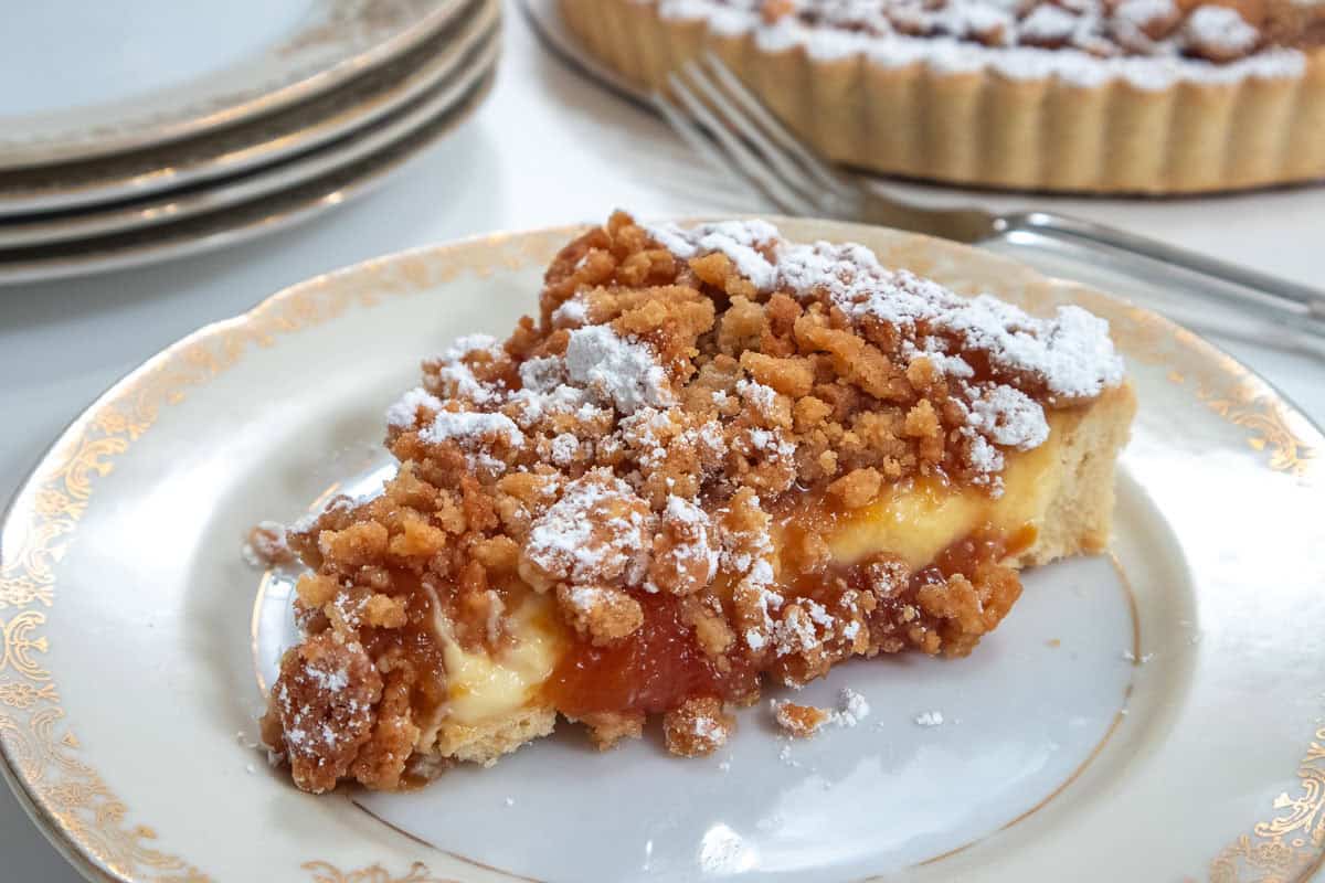 A slice of the Caramelized Peach Tart sits on a antique plate with more plates and the tart in the background 