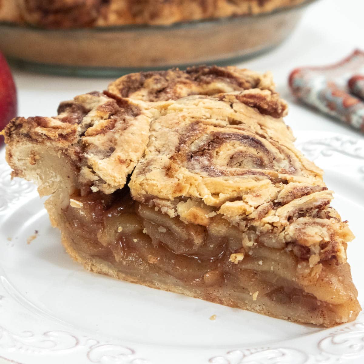 Cinnamon Bun Apple Pie slice on a plate with the pie plate in the background.