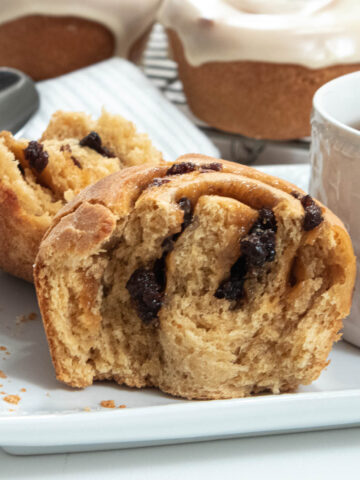 Rum Raisin Rolls on a plate with a cup of tea and an iced roll in the background