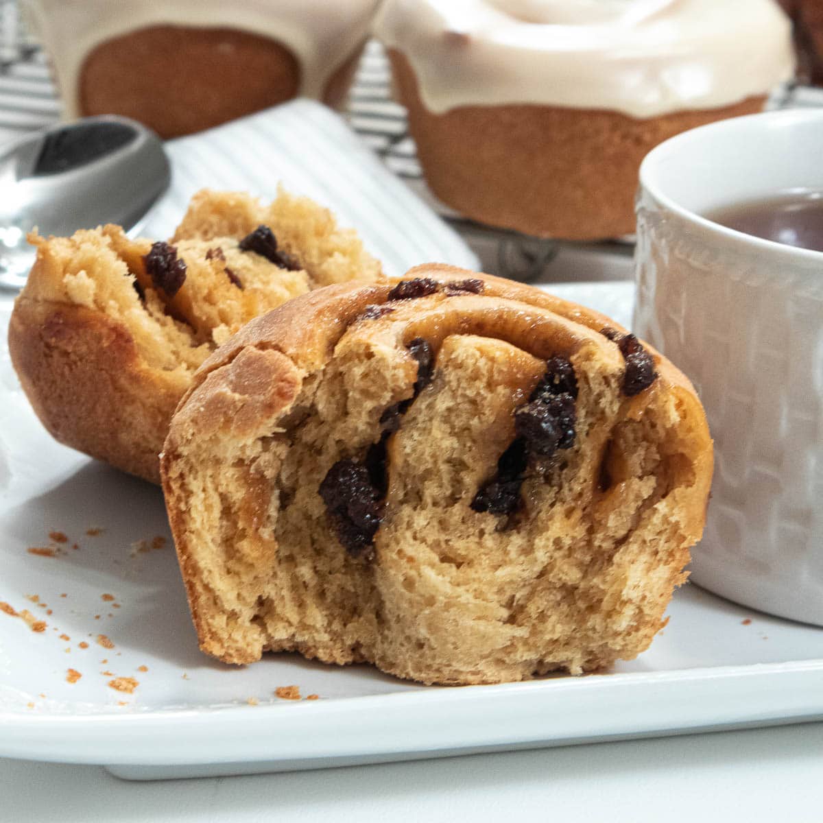 Rum Raisin Rolls on a plate with a cup of  tea and an iced roll in the background