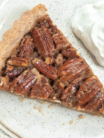 A slice of Butter Rum Pecan Tart on a plate with whipped cream to the side.