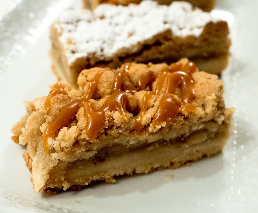 Apple crumb bars with caramel drizzle and finished with powdered sugar.