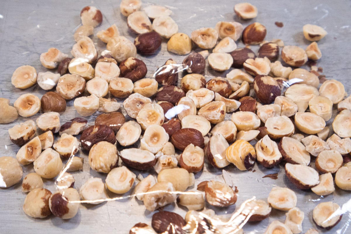 Hazelnuts on a sheet pan covered with plastic wrap.