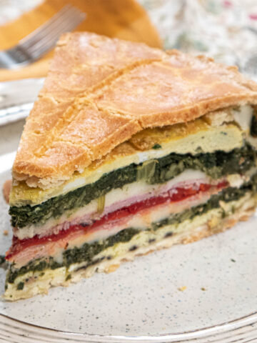 A slice of Tourte Milanese sits on a plate exposing its dramatic yellow, green, red and pink layers.
