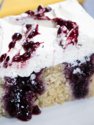 Blueberry poke cake is a 9x13" cake that has holes poked in it and filled with a blueberry compote. It is finished with whipped cream and blueberry filling