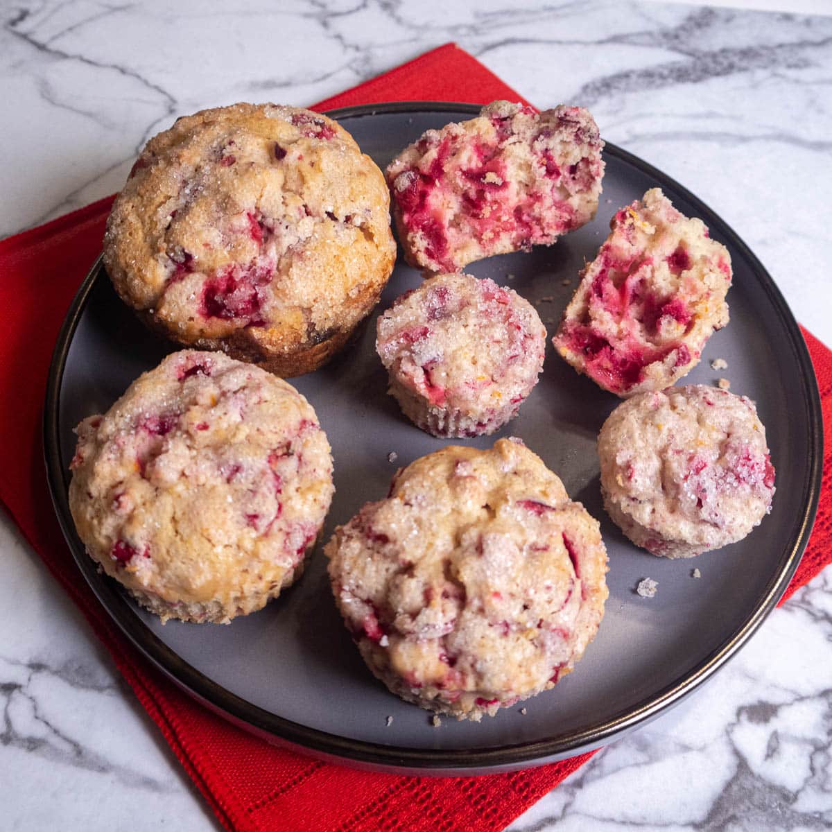 Cranberry Orange Muffins in three sizes, mini, regular and Texas on a gray plate with a red napkin.
