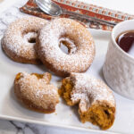 Pumpkin cake donuts on a plate with a cup of tea.