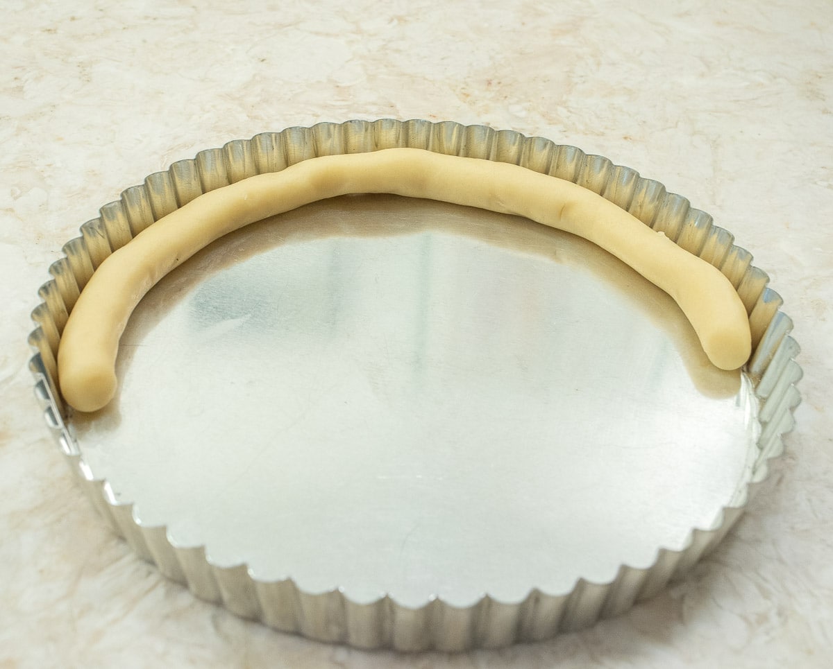 The rope of pastry has been placed on one side of the tart pan.