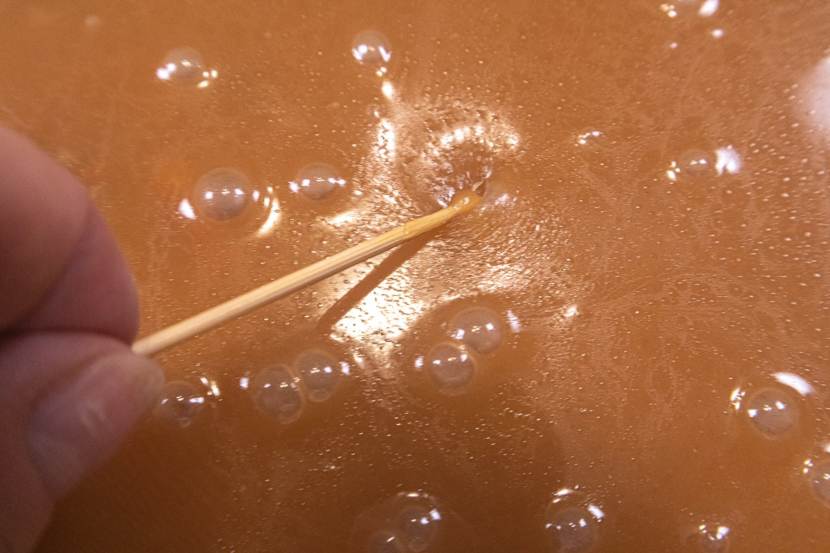 Using a toothpick to break the air bubbles on the caramel layer of the Chocolate Caramel Pecan Tart