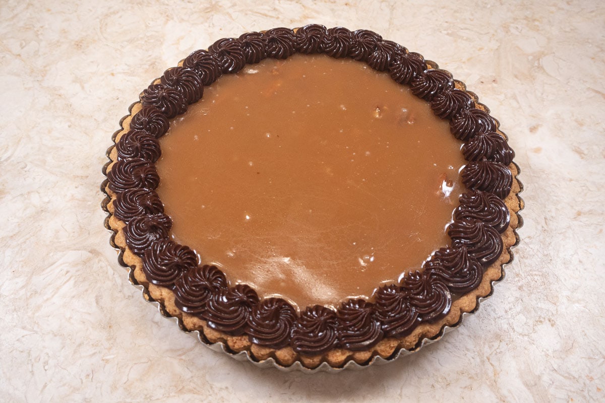 The completed tart in its pan is finished with a caramel top wreathed in chocolate ganache