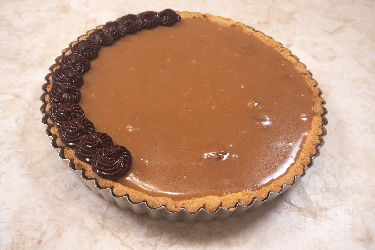 Piping chocolate ganache around the edge of the Chocolate Caramel Pecan Tart