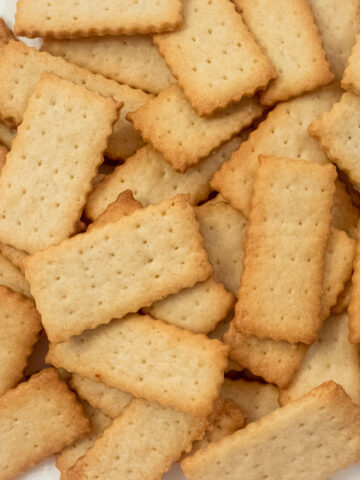 A bunch of French Butter Cookies, Petit Beurre, on a plate. They are rectangular cookies with holes throughout them and have browned edges