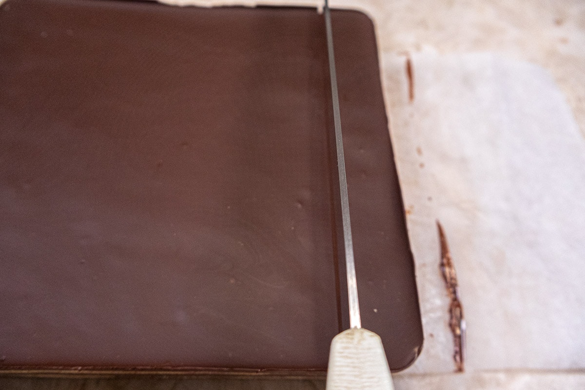 A dry, hot knife melts through the chocolate layer and cuts straight down.