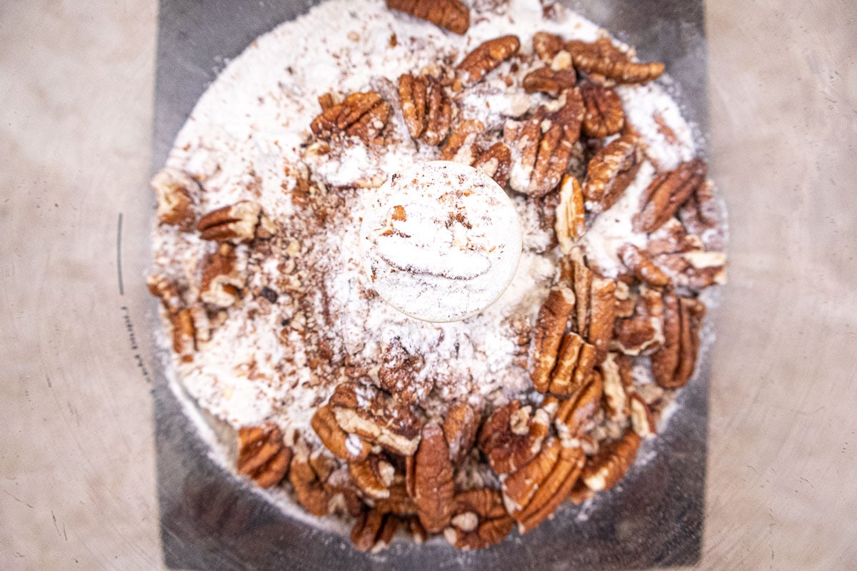 The toasted pecans and flour are placed in the bowl of a food processor.